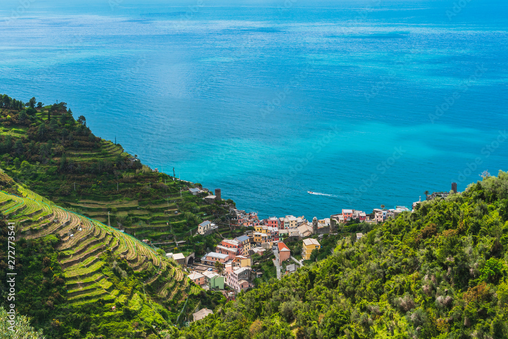 View over the old charming village of Vernazza in Cinque Terre, Italy, on a summer day. Vibrant landscape with green forest, terraced hills, turquoise sea waters and colorful houses.