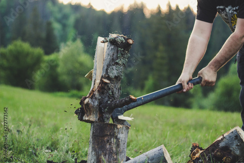 The guy is cutting an old tree in the mountains with an ax. Ukrainian Carpathian Mountains. Bonfire. Tourism. Ax