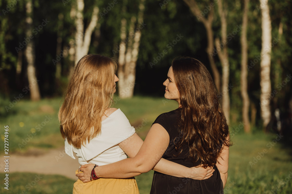 Young women different build with long hair are embracing on the green field in the evening. Friendship, sisters, nontraditional family, bodypositive, natural authentic beauty, summer vacation, blonde Young women different build with long hair are embracing on the green field in the evening. Friendship, sisters, nontraditional family, bodypositive, natural authentic beauty, summer vacation, blonde