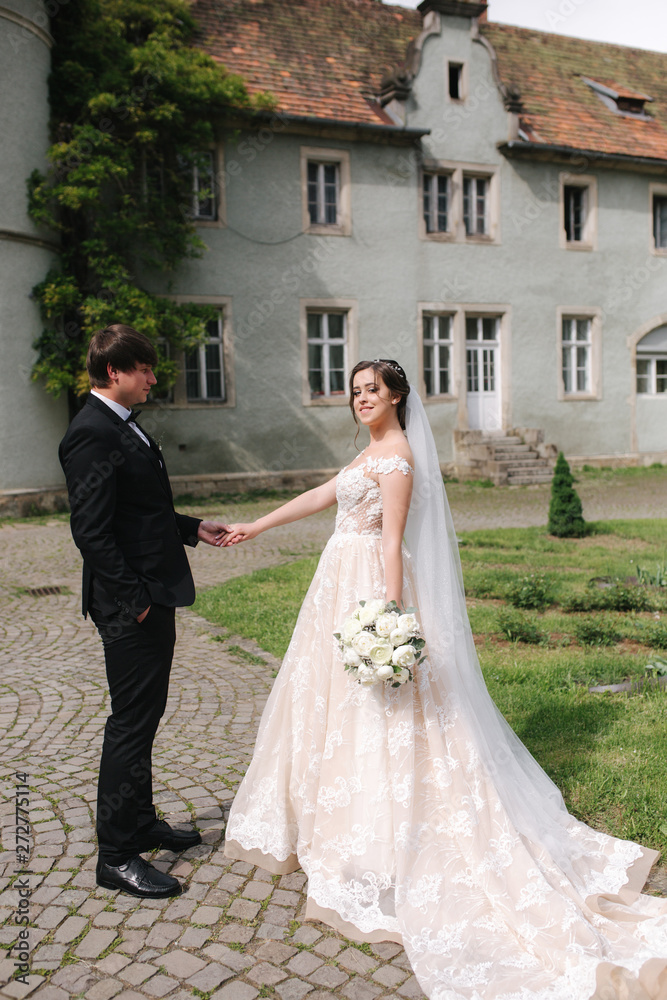 Fototapeta premium Newlyweds are walking in the park near the big castle. Beautiful bride with handsome groom