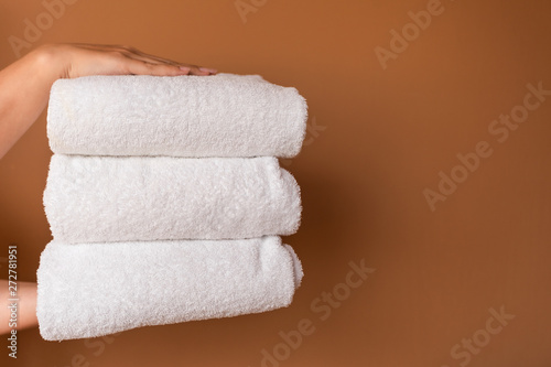 Closeup view of two female hands holding stack of 3 white towels isolated on brown background. Horizontal color photography.