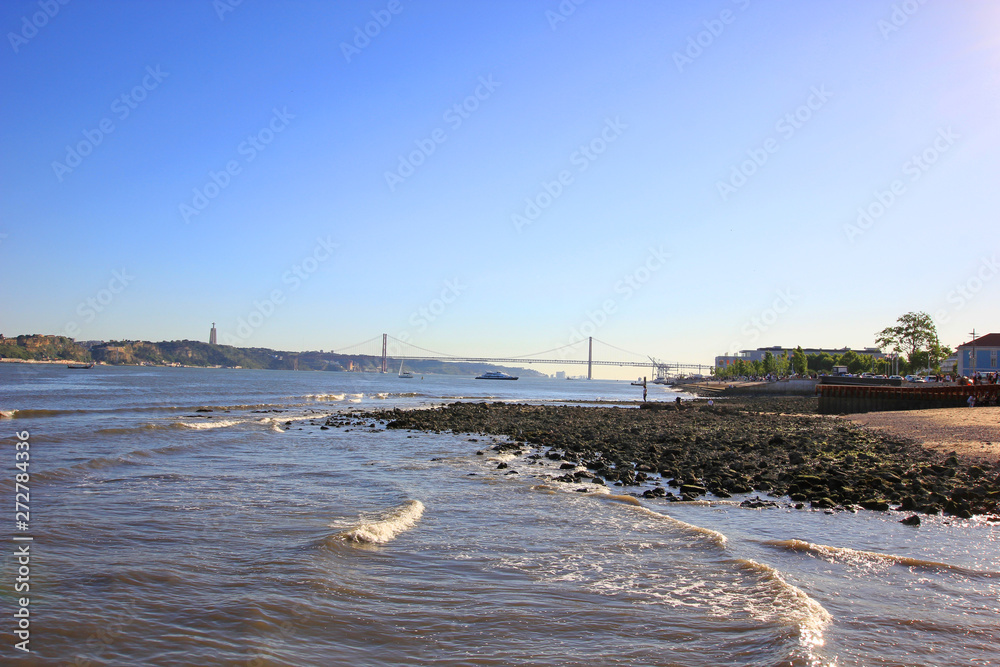 river coast in lisbon portugal, with the 25 de abril bridge in the background