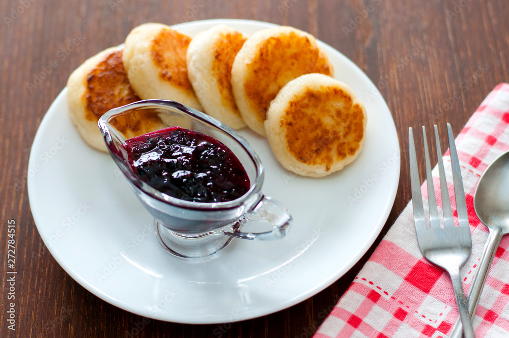 Cheese pancakes with currant jam, on a white plate with a fork, a teaspoon and a napkin, view from the top. Cheese pancakes with currant jam, on a white plate with a fork, a teaspoon and a napkin, view from the top.