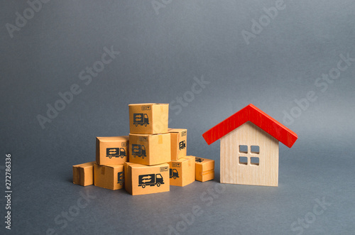 A pile of cardboard boxes and a wooden house. Concept of moving to another house or city. Property transportation. Freight shipping, delivery and installation. The beginning of a new stage of life