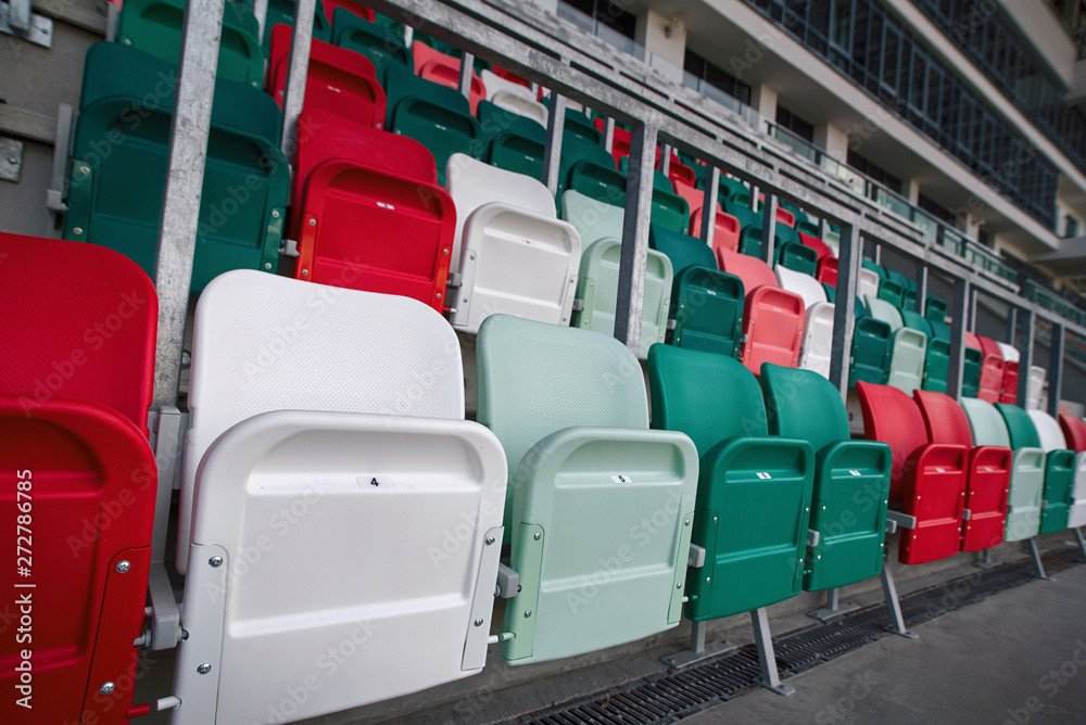 Fototapeta premium Rows of empty multicolored plastic stadium seats. Empty seats on tribune arena. Football stadium bleachers. Soccer, football stadium tribune without fans. Empty tribunes, game over. Sport Concept