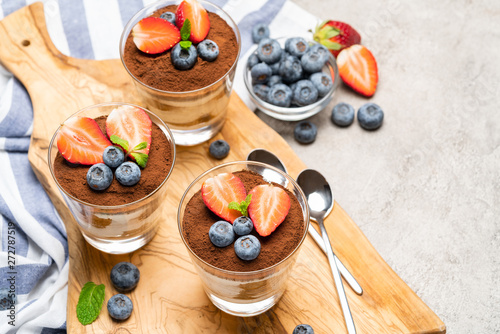 Classic tiramisu dessert with blueberries and strawberries in a glass on concrete background