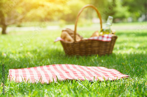 Fototapeta Naklejka Na Ścianę i Meble -  Wicker picnic basket with food and red tablecloth on the grass.
