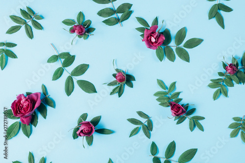 Summer minimal concept. Pattern made of red rose flowers and green little leaves on blue background. Many little leaves for decorating any post card or celebration card. Flat lay, top view