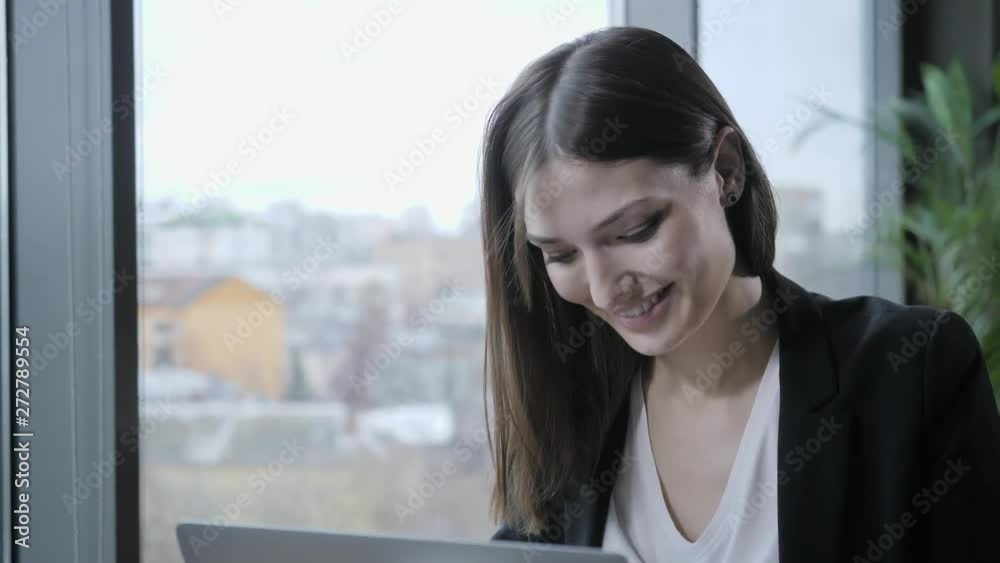 Young woman laughs and smiles, Sitting in coffee shop at wooden table. On table is gray aluminum laptop. Girl blogging, browsing internet, chatting Young woman laughs and smiles, Sitting in coffee shop at wooden table. On table is gray aluminum laptop. Girl blogging, browsing internet, chatting