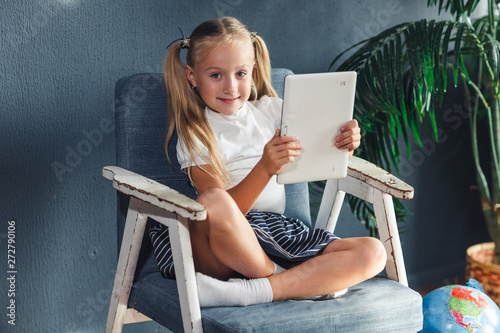Technologies, people concept - young blondy girl sitting on a chair and watching the tablet or surfing the net and smiling.