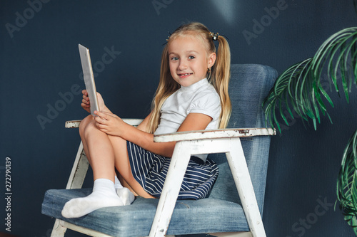 Cute little girl playing with tablet. Happy blondy girl at home. Funny lovely girl having fun in kids room.