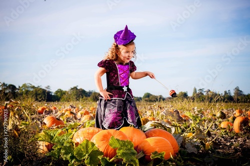 Happy Halloween! Cute cheerful little witch with a magic wand. Beautiful child girl in witch costume sitting on the big pumpkin, conjuring and laughing.