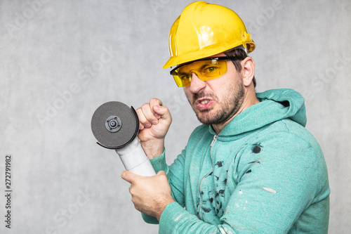 the construction worker holds an angle grinder in his hand