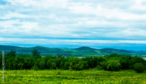 Cloudy blue sky on the horizon of Russian fields and mountains. Summer forest on a sunny day.