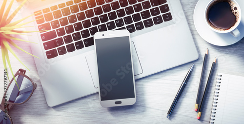 Fotografie Smartphone und Laptop auf hellem Schreibtisch im Sonnenlich