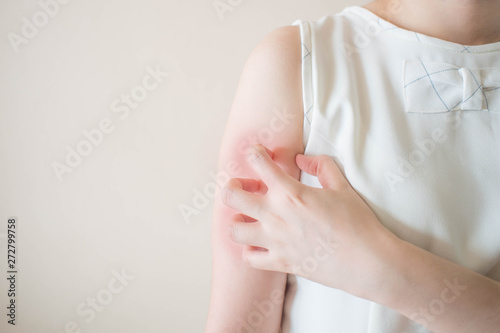 Young woman scratching arm from having itching on white background w/ copy space. Cause of itchy skin include insect bites, dermatitis, food/drugs allergies or dry skin. Health care concept. Close up.