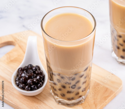 Popular Taiwan drink - Bubble milk tea with tapioca pearl ball in drinking glass on marble white table wooden tray background, close up, copy space