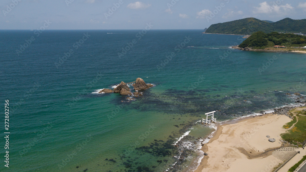 Obraz premium aerial footage of blue ocean, white wave and the twin rocks through the torii gate at the coast of sakurai futamigaura beach, itoshima fukuoka japan