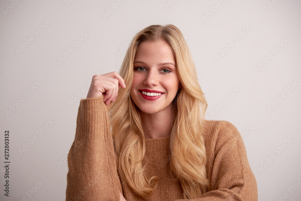 Cheerful young woman with blond hair and red lipstick sitting at isolated background