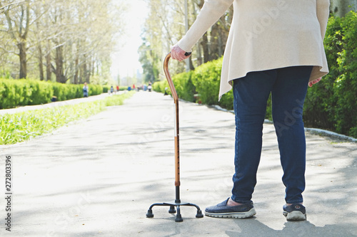 Senior disabled caucasian woman hands on cane outside nursing home park. Close up of elderly lady holding a walking stick outdoors of healthcare facility on the sunny day. photo