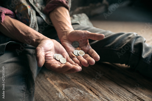Male beggar hands seeking money, coins from human kindness on the wooden floor at public path way or street walkway. Homeless poor in the city. Problems with finance, place of residence.