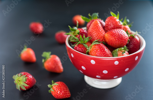 Delicious strawberries in a bowl on black background.