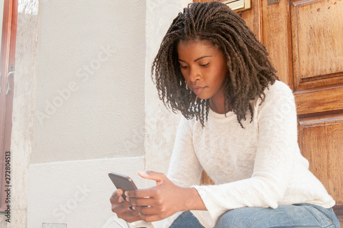 Canvas-taulu Serious pensive black girl surfing net on smartphone outdoors