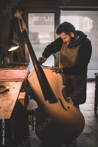 Young luthier working in his workshop, building a double bass photo