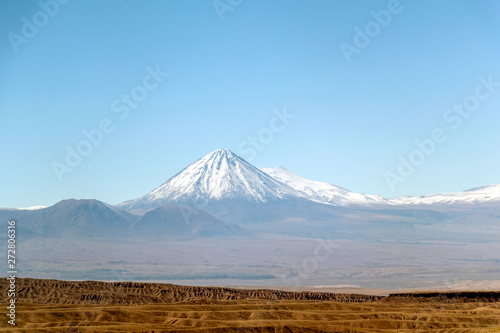 Blurred background of Atacama Desert landscape with snow-capped Andean volcanos, salt flat and some vegetation on horizon, Chile