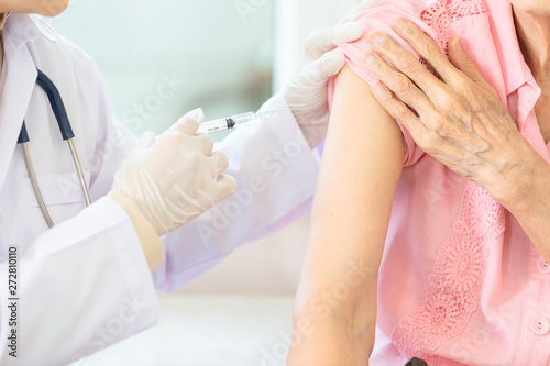 Close up,asian female doctor with syringe doing injection vaccine,flu,influenza in the shoulder of senior woman, nurse injecting,vaccinating elderly patient,vaccination,medicine,health care concept © Satjawat