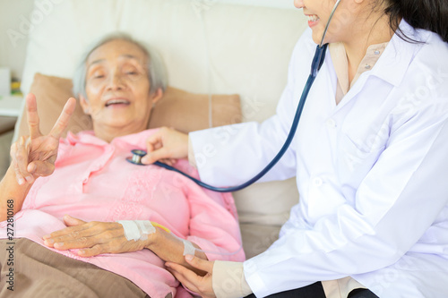 Medical female doctor or nurse checking senior patient using stethoscope in hospital,closeup hand of elderly asian woman showing two fingers,v-sign,feel so happy and smile,health care,support concept