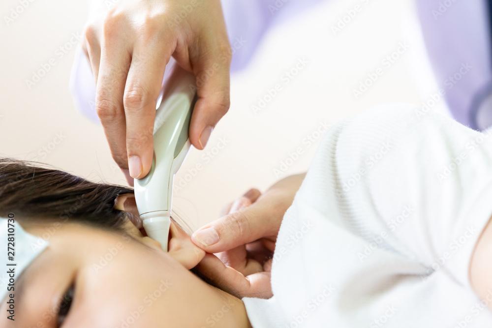 Closeup of hand doctor or nurse checking child patient temperature in the ear using digital thermometer,asian little girl having fever using cold gel placed on her forehead to relief fever,headache Closeup of hand doctor or nurse checking child patient temperature in the ear using digital thermometer,asian little girl having fever using cold gel placed on her forehead to relief fever,headache