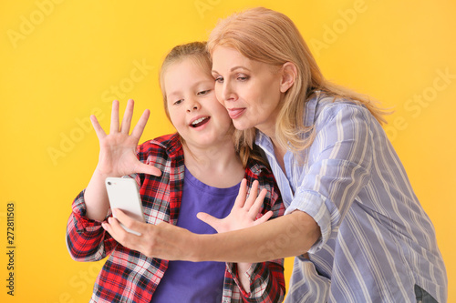 Mature woman and her cute granddaughter taking selfie on color background