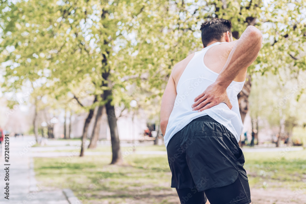 back view of sportsman suffering from pain while touching injured back back view of sportsman suffering from pain while touching injured back