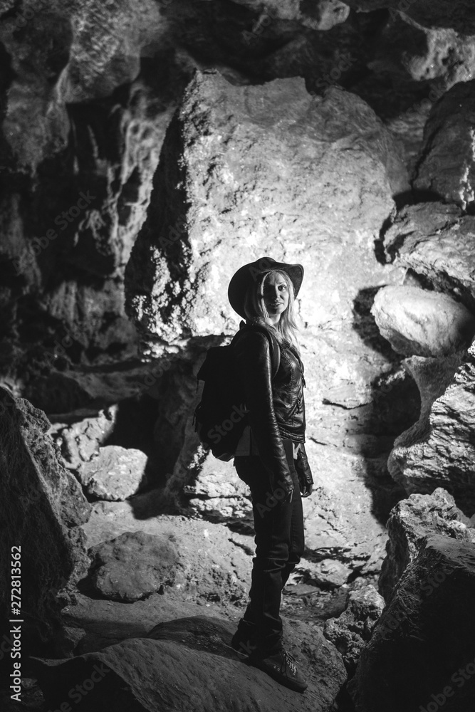 Obraz premium Girl exploring huge cave. Adventure traveller dressed cowboy hat and backpack, leather jacket. black and white, tourist route. ancient crystal formations, vertical photo, village Kryvche. Ukraine