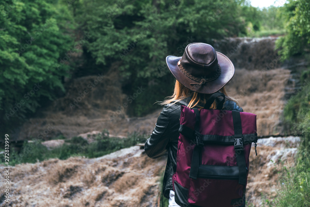 Young european female tourist with backpack and cowboy hat looking at the river washed away the bridge, the crossing was impossible. Deep waterfall. Copy space. adventure concept. active lifestyle