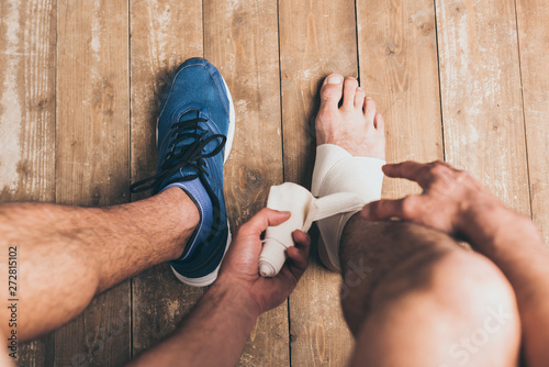 cropped view of sportsman in one sneaker bandaging injured leg with elastic bandage