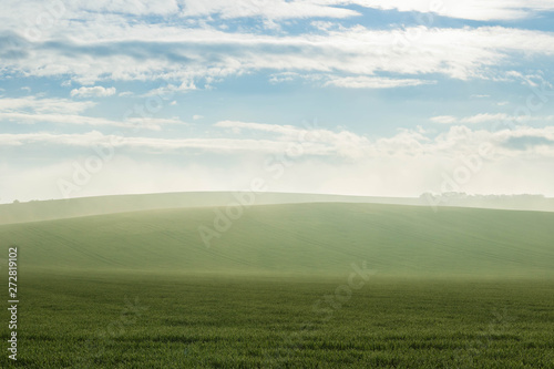 Foggy landscape against the sunlight of the early morning with field of grass in the foreground