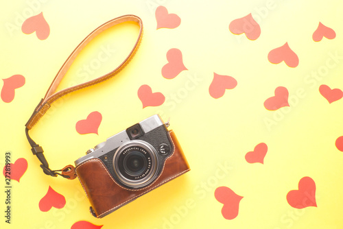 Retro style photo camera and red paper hearts on yellow background. Love concept.