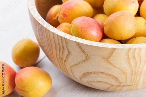 ripe organic apricots fruits in ash tree wooden bowl on a white wooden background