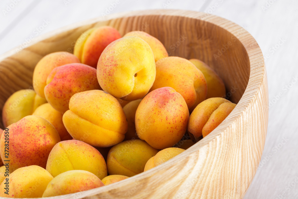 ripe organic apricots fruits in ash tree wooden bowl on a white wooden background ripe organic apricots fruits in ash tree wooden bowl on a white wooden background