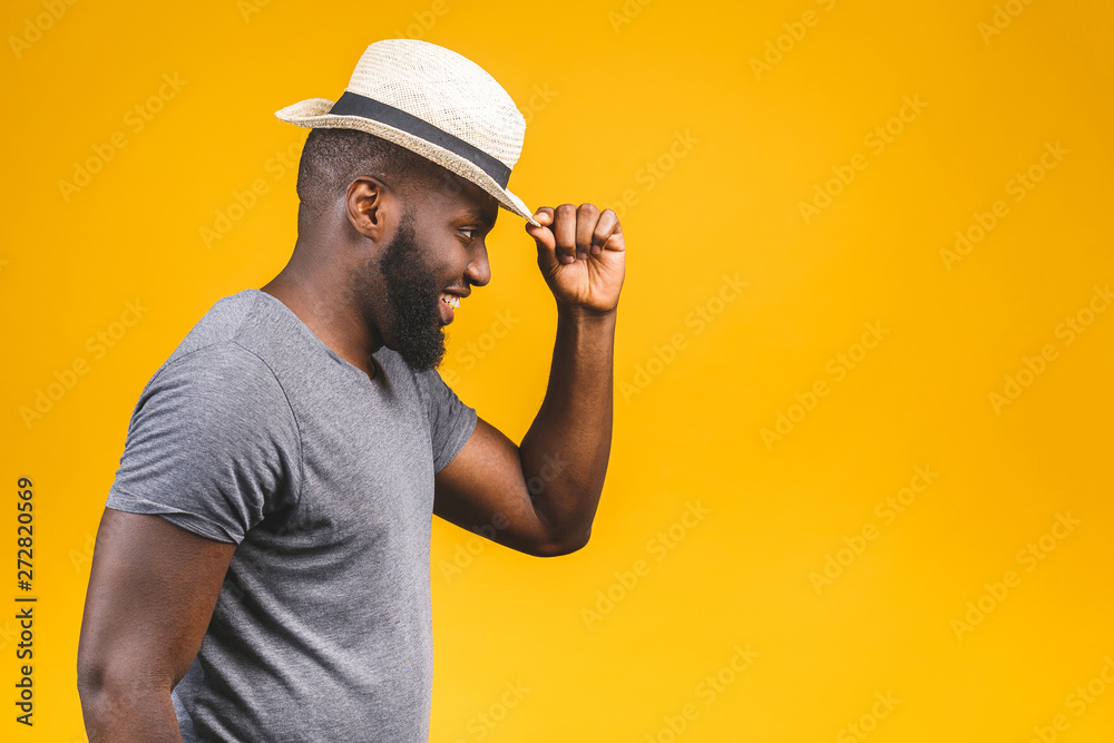 Cheerful carefree young dark-skinned african american man with trendy hat smiling, posing isolated against yellow wall with copy space for your content.