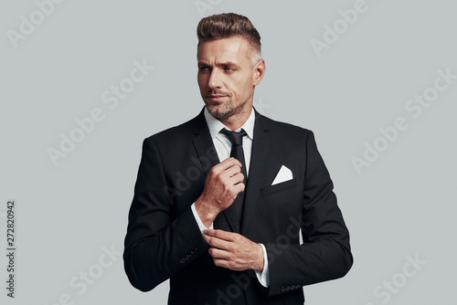 Confident in his style. Handsome young man adjusting his sleeve while standing against grey background