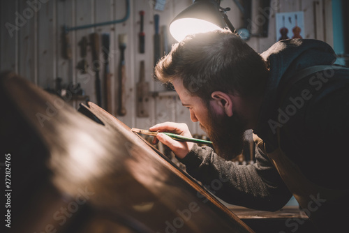Young luthier working in his workshop, building a double bass