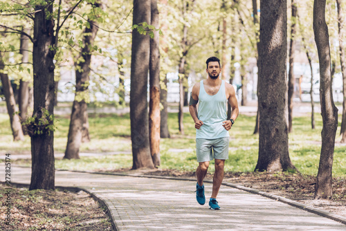 handsome sportsman jogging along walkway in green sunny park
