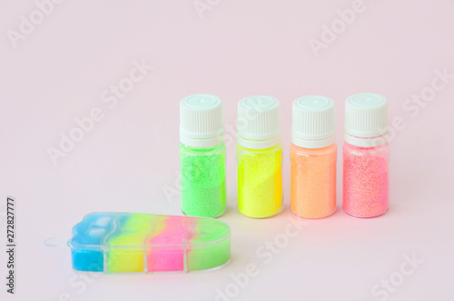 Colorful glitters lies on pastel pink background. Many round jars with multi-colored bright sparkles for nail polish. Sparkling sequins