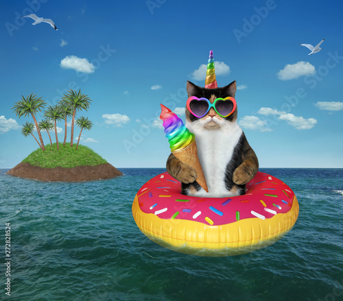 The cat in sunglasses eats rainbow ice cream on the inflatable circle near the the small desert island in the open sea. © iridi66