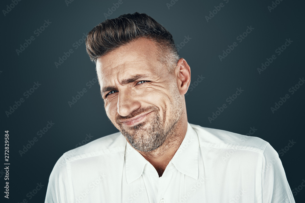 Confusion. Displeased young man grimacing and looking at camera while standing against grey background Confusion. Displeased young man grimacing and looking at camera while standing against grey background