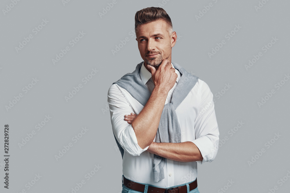 Confidence and charisma. Handsome young man looking away and smiling while standing against grey background