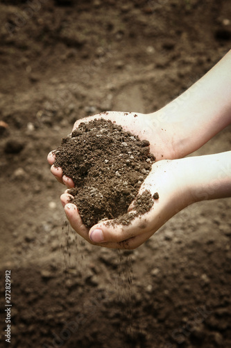 Children's hands hold in a handful of brown soil that falls slightly down.